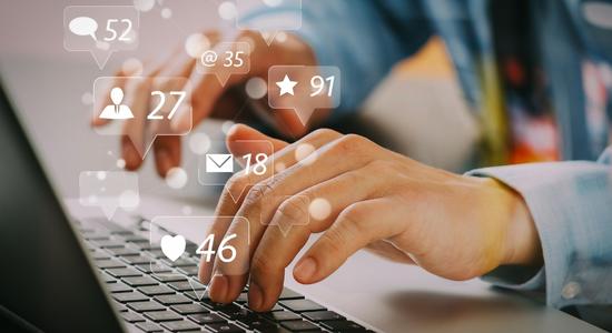 Close-up of man hands typing on laptop keyboard with likes, followers, messages graphics hovering above. 