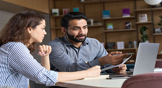 Man and woman working on laptop in office. 