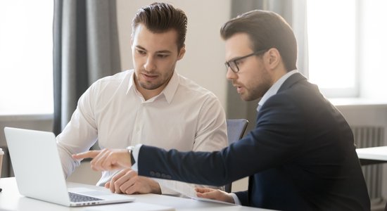 Two men working together discussing something on a laptop at a desk. Concept of marketing translation company.