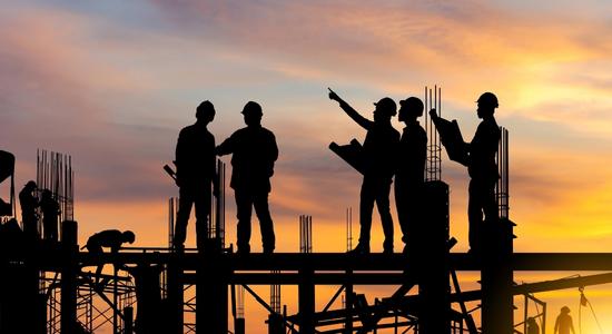 The silhouettes of five engineers discussing on a construction site at sunset. Concept of civil engineering translations.