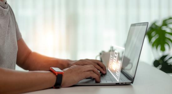 Close-up of a man's hands typing on laptop, illuminated graphic hovering above. 