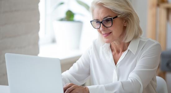 A blonde woman in a white shirt smiling at a computer. 
