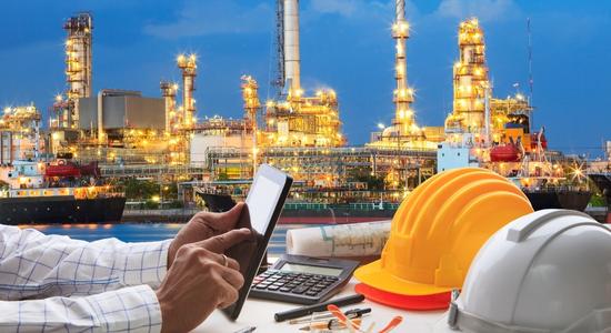 A man working at a desk, well-lit oil rig in the background. 