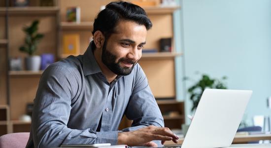 A smiling man working on a laptop in daylight. 