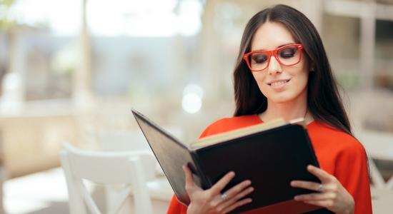 A woman in red shirt and glasses smiling at menu in hand. Concept of food and beverage translation.