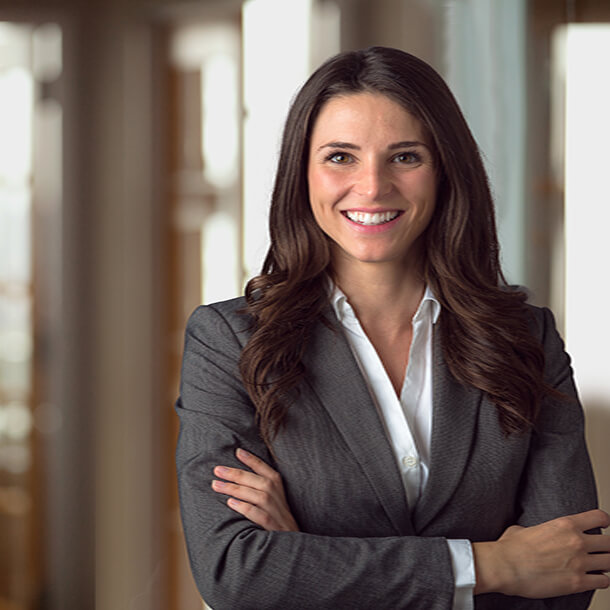 A professional smiling businesswoman standing in office with folded hands.