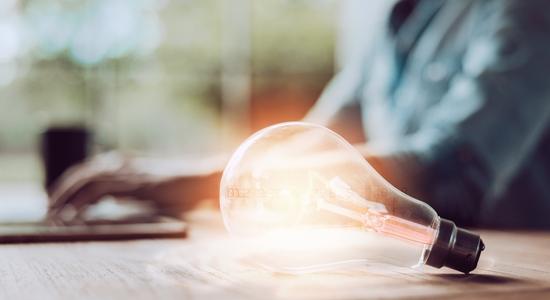 An illuminated lightbulb lying on a desk, man working in background. Concept of intellectual property translation.