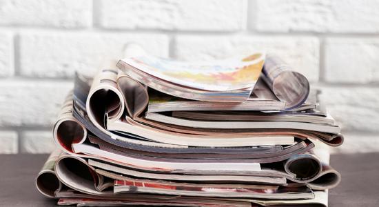 Stack of open magazines and catalogues in front of white brick wall. 