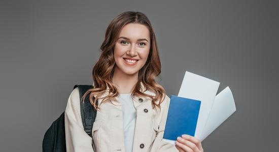 A woman smiling at camera holding up passport and paperwork. 