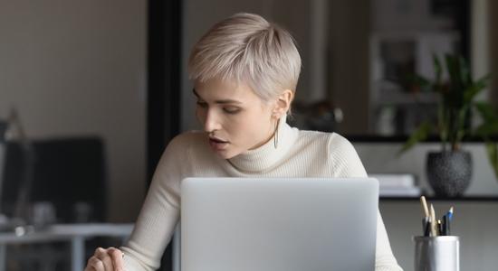 A woman with a blonde pixie cut working with paperwork and laptop. Concept of patent translators.