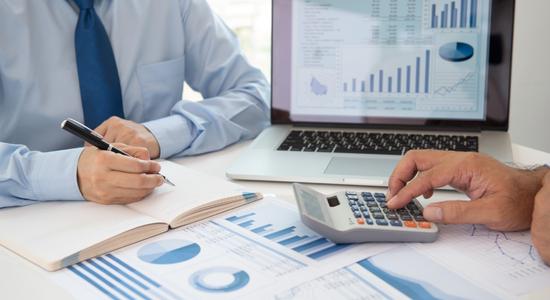 Two men work on financial sheets using calculator and pen to take notes.