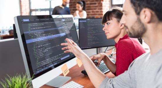 A man and woman looking and pointing at code on a computer. Concept of translating software.