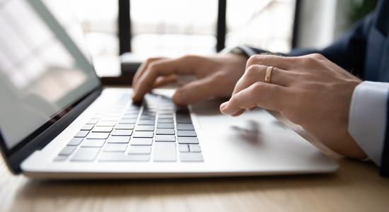Two hands typing on a key board, a golden ring in focus. Concept of email translation and letter translation.