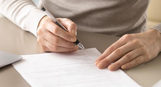 A person signing a contract on a desk with a black pen. Concept of legal contract translation services..