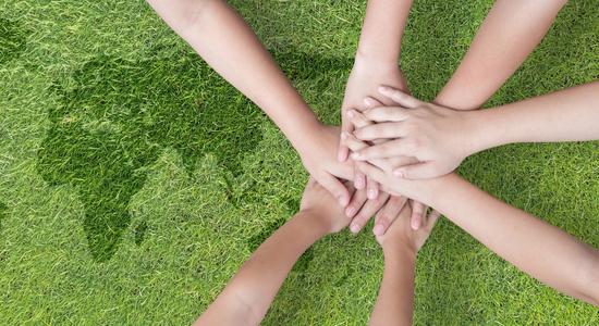Several hands stacked on top of each other, over grass world map. Concept of environment translation services.