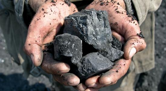 A miner's cupped hands holding out lumps of gray coal. 