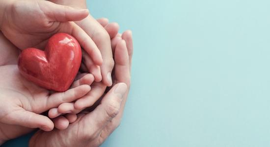 Several hands on top of each other holding a red heart figure.