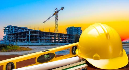 A yellow hard hat and engineering supplies with construction site in background.