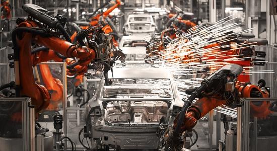 Orange robotic machines working on car chassis in an assembly line. 