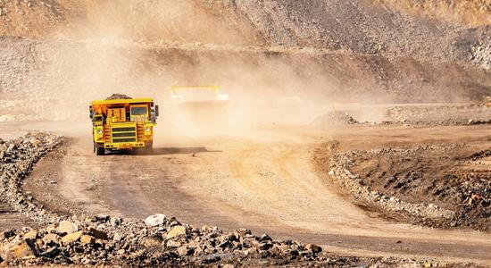 Two large yellow construction vehicles driving through a dirt quarry. Concept of machinery translation services.