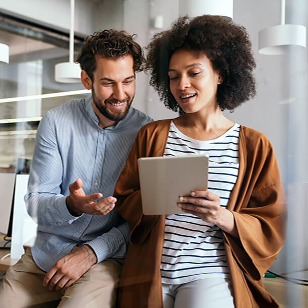 Two young employees celebrate success by giving high-five while their colleagues sitting and smiling. 