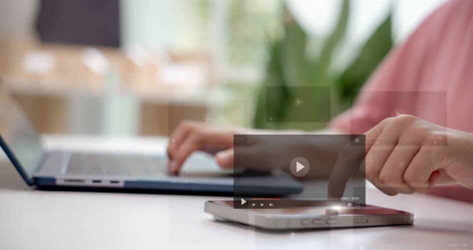Hands of a woman using a laptop with video play icons and a smartphone. a notion of contemporary communication technology, online media marketing, and video translation services.