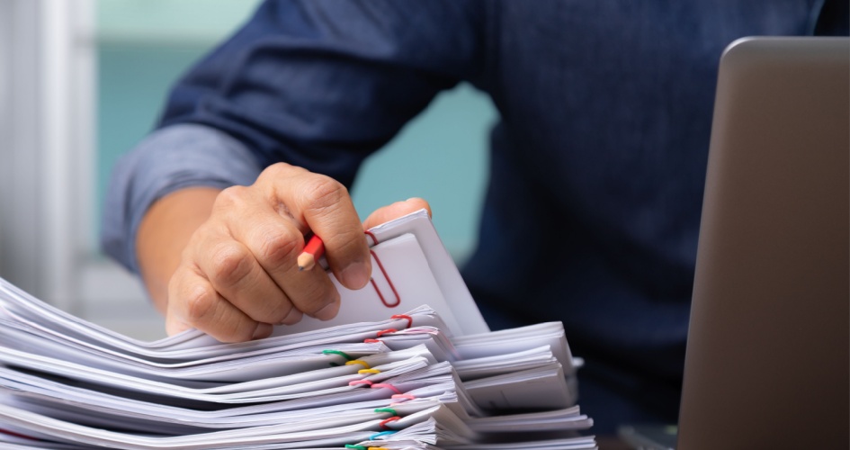 Businesswoman working with stacks of paper files to search for technical documents at busy desk in office. A concept of technical translation services.