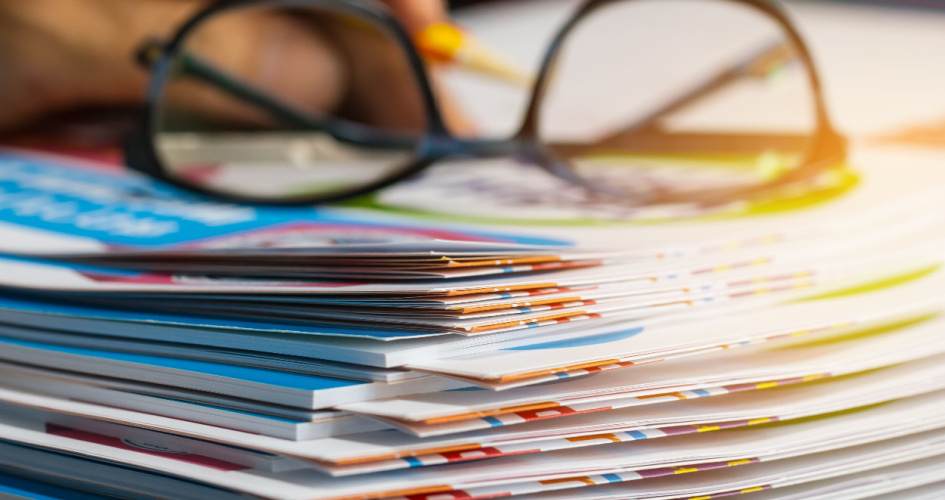 A pile of colourful report paper documents for business office with glasses. A concept of language transcreation services.